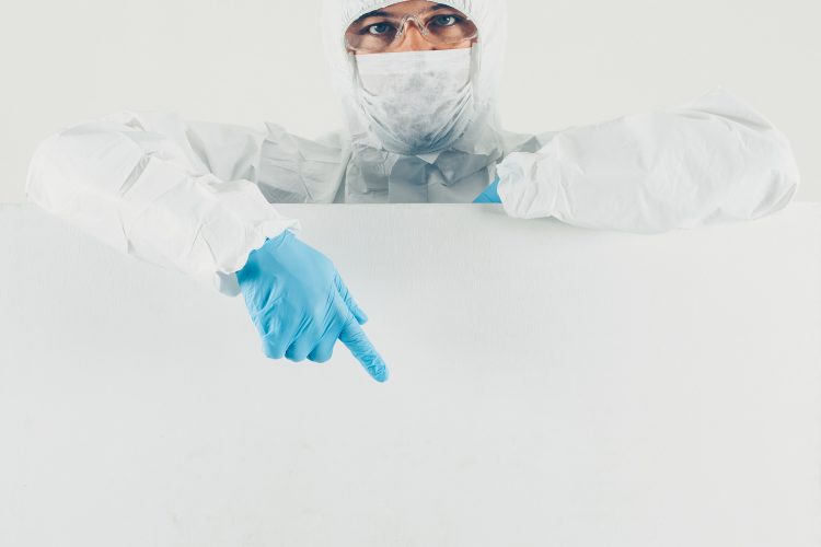 A doctor in mask, gloves and protective suit pointing down in white background . space for text. coronavirus
